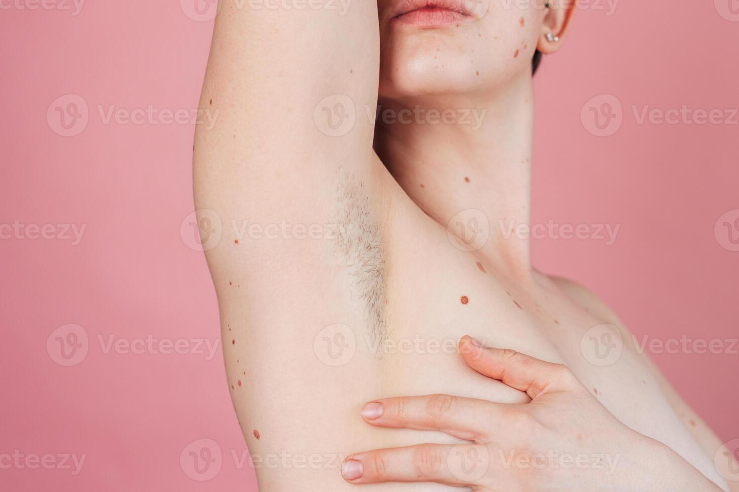 A young beautiful shirtless woman showing off her hairy armpits on an isolated pink background. photo