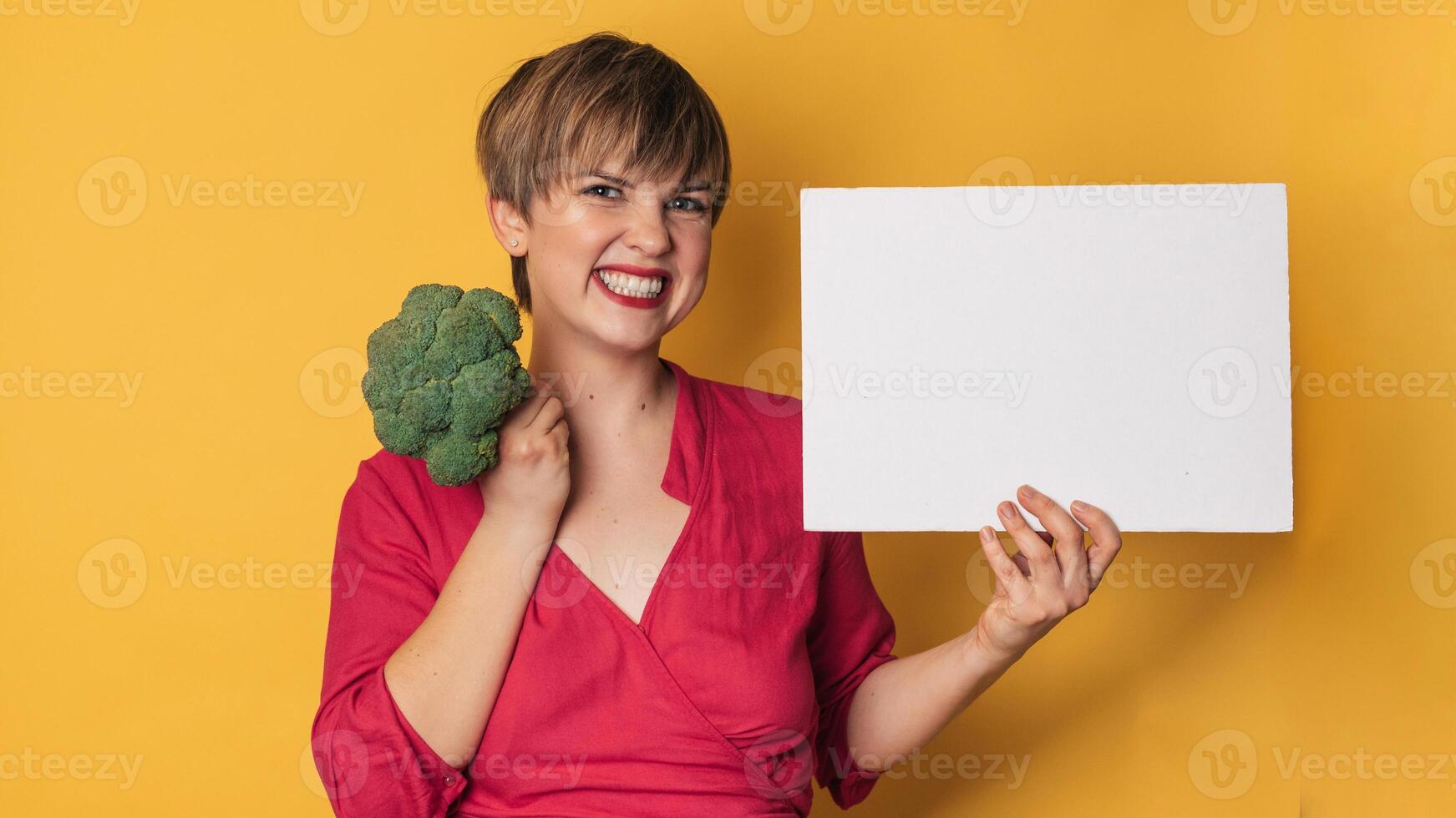 A studio shot of a young smiling woman holding fresh broccoli and a blank letterhead. The concept of healthy eating. A place for your text. Panoramic banner. photo