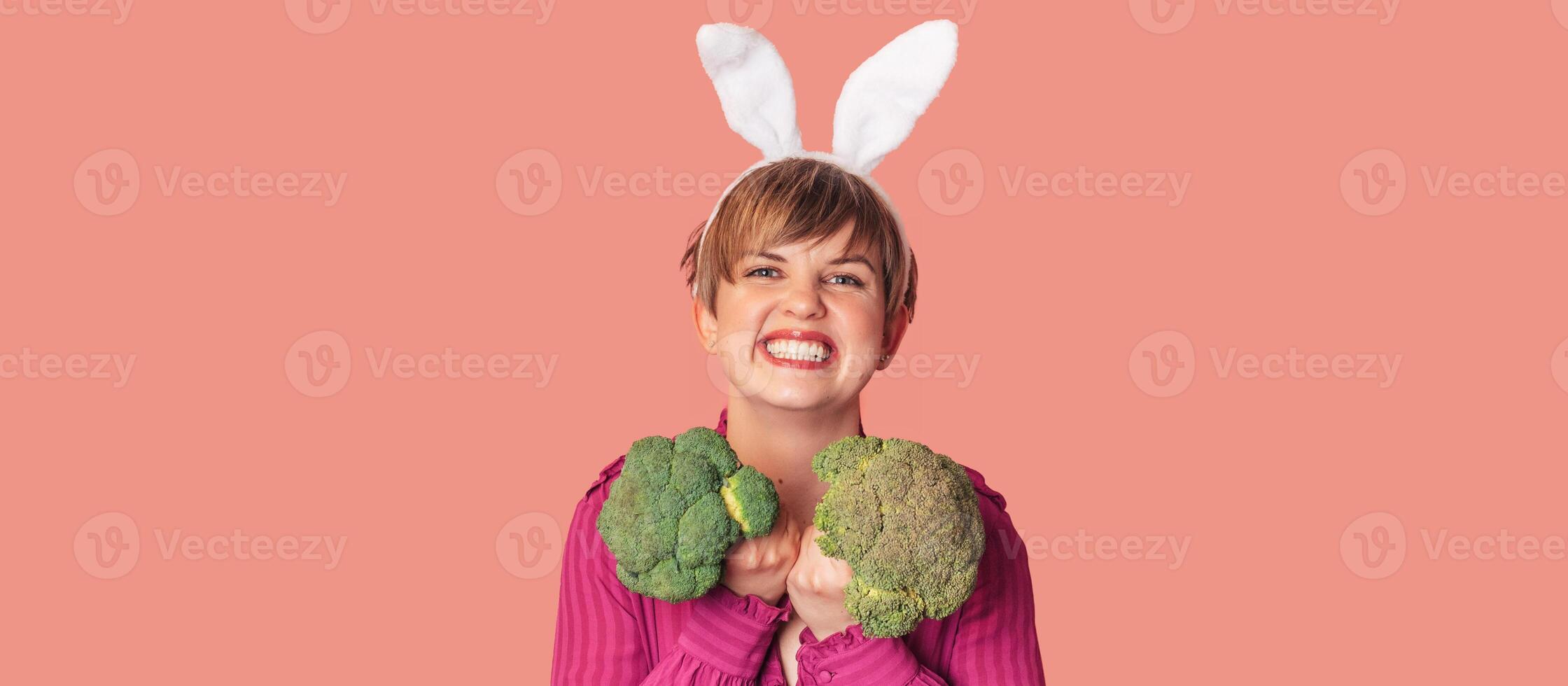 Studio shot of a young Caucasian woman in bunny ears holding fresh broccoli in her hands. healthy eating.A panoramic banner with a copy of the space. photo