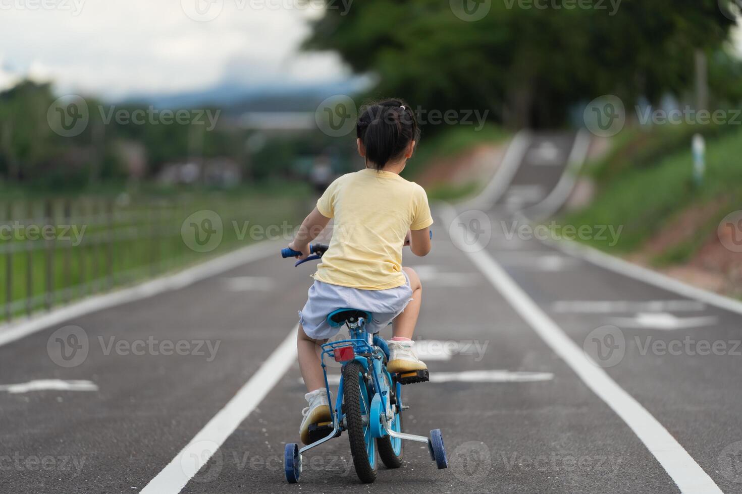 Back side view of asian baby girl child learning to ride bicycle in the park garden. Education concept for kid practiice cycling at park, baby sport concept. photo