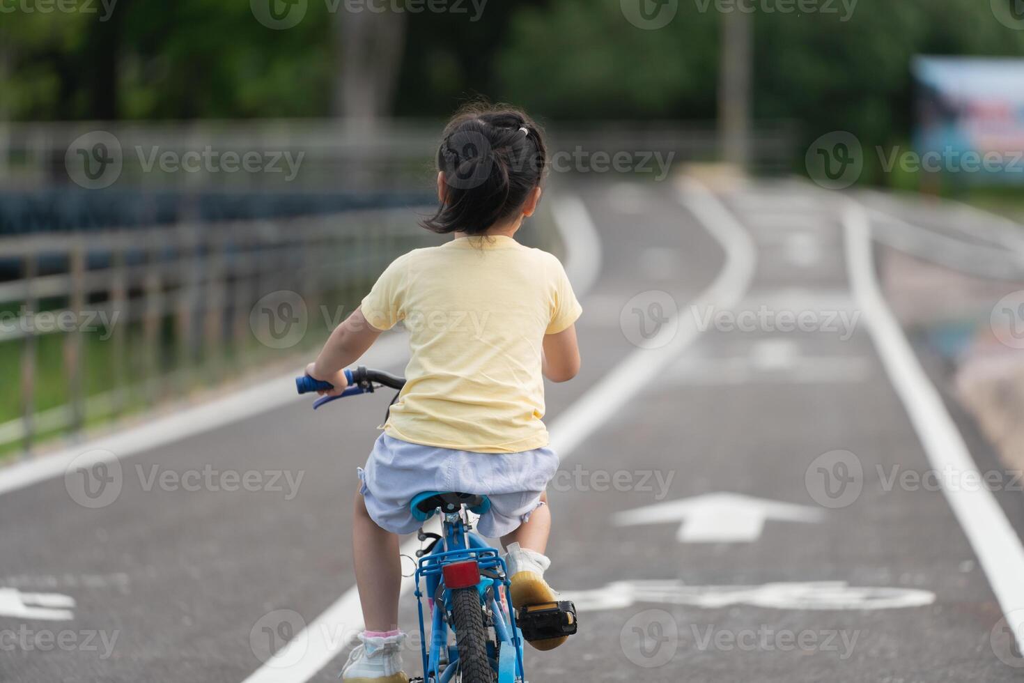 Back side view of asian baby girl child learning to ride bicycle in the park garden. Education concept for kid practiice cycling at park, baby sport concept. photo