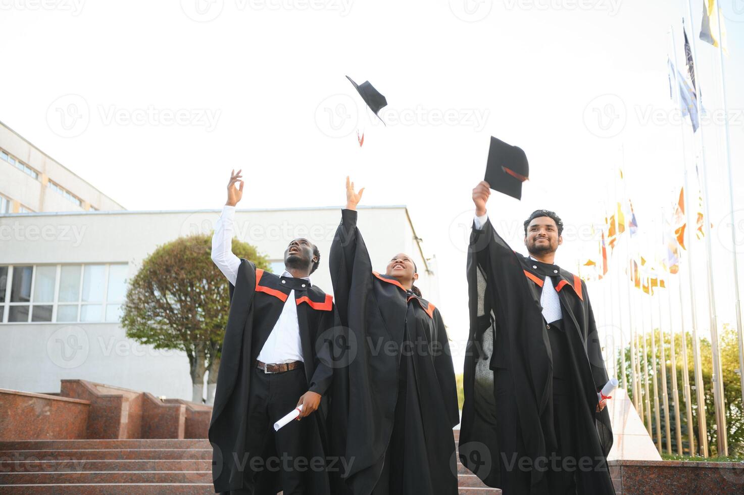 group of happy international students in bachelor gowns throwing mortar boards up photo