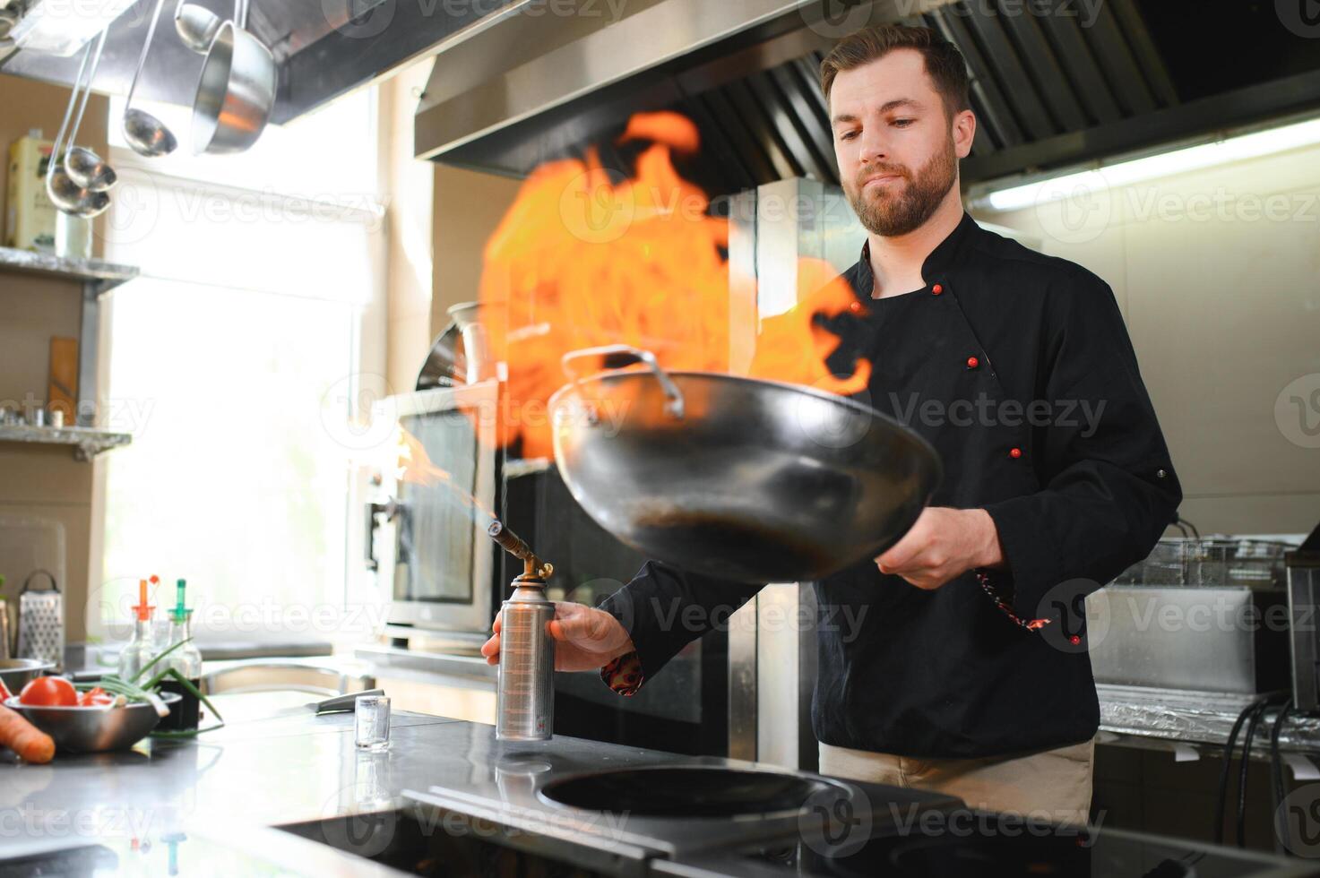 Chef in restaurant kitchen at stove and pan cooking flambe on food photo