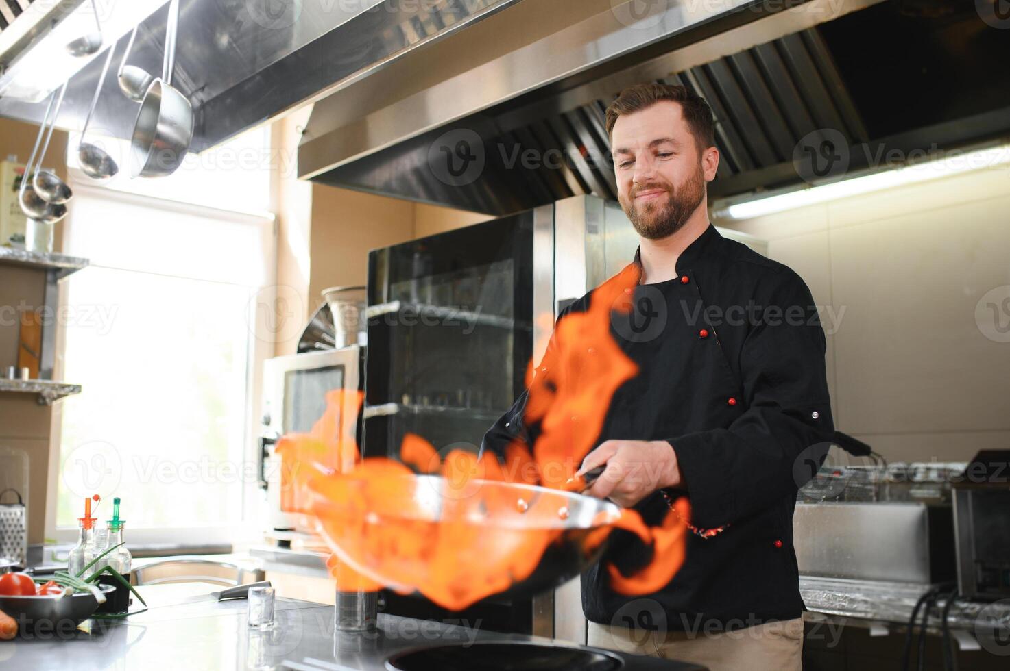 Chef in restaurant kitchen at stove and pan cooking flambe on food photo