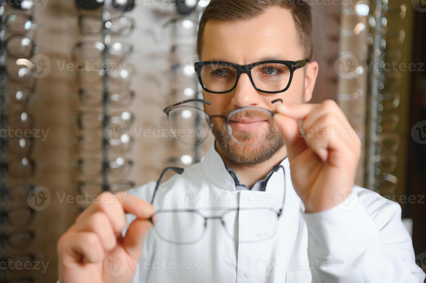Handsome ophthalmologist holding eyeglasses for a try out. Optometrist offering to wear a pair of glasses. photo
