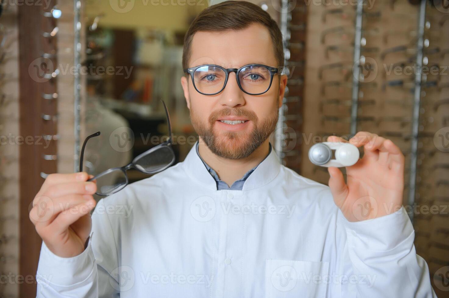 Male doctor holding contact lens case and glasses, indoors photo