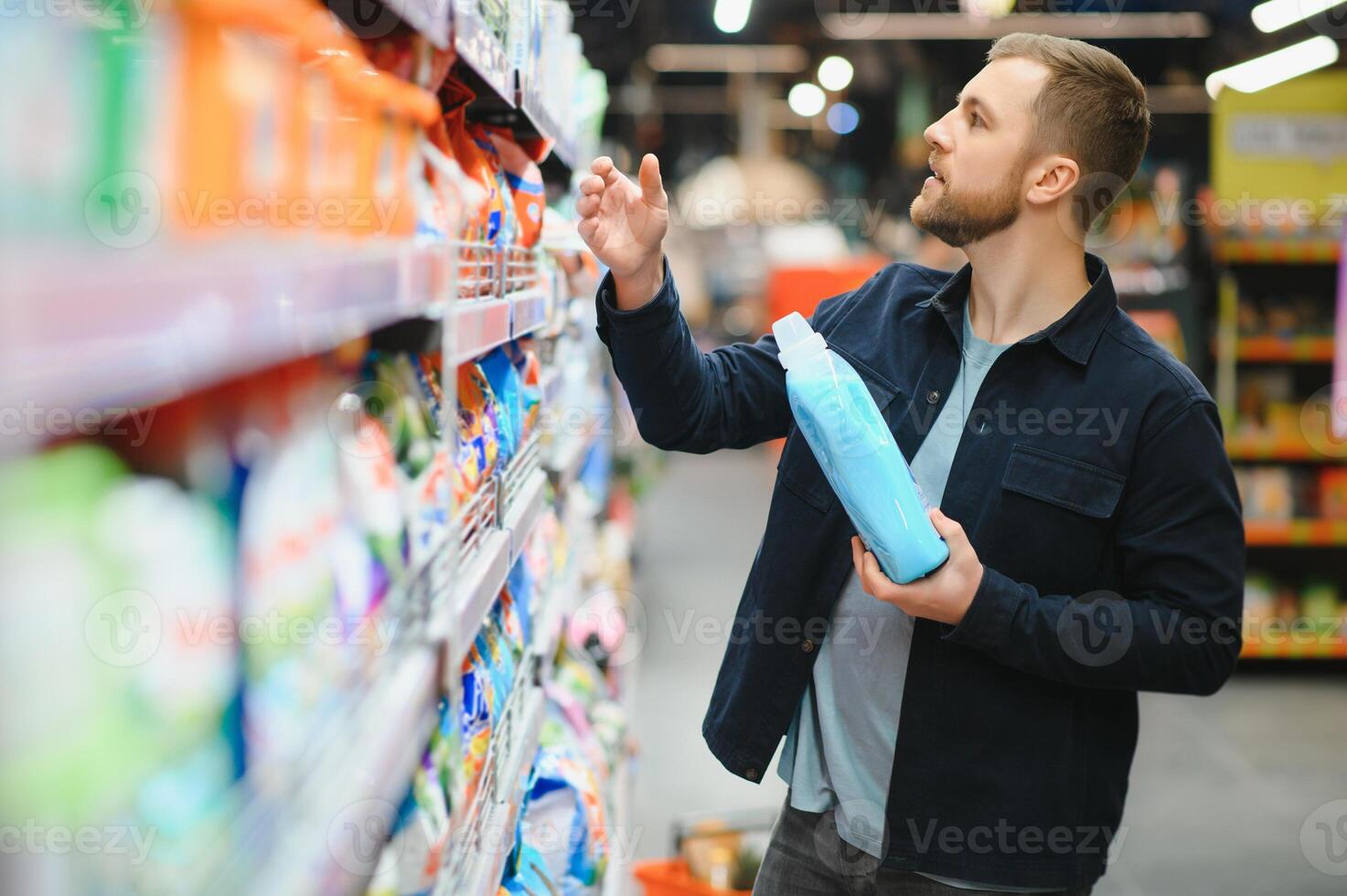 Young cheerful positive male customer making purchases in supermarket, buying household chemicals photo