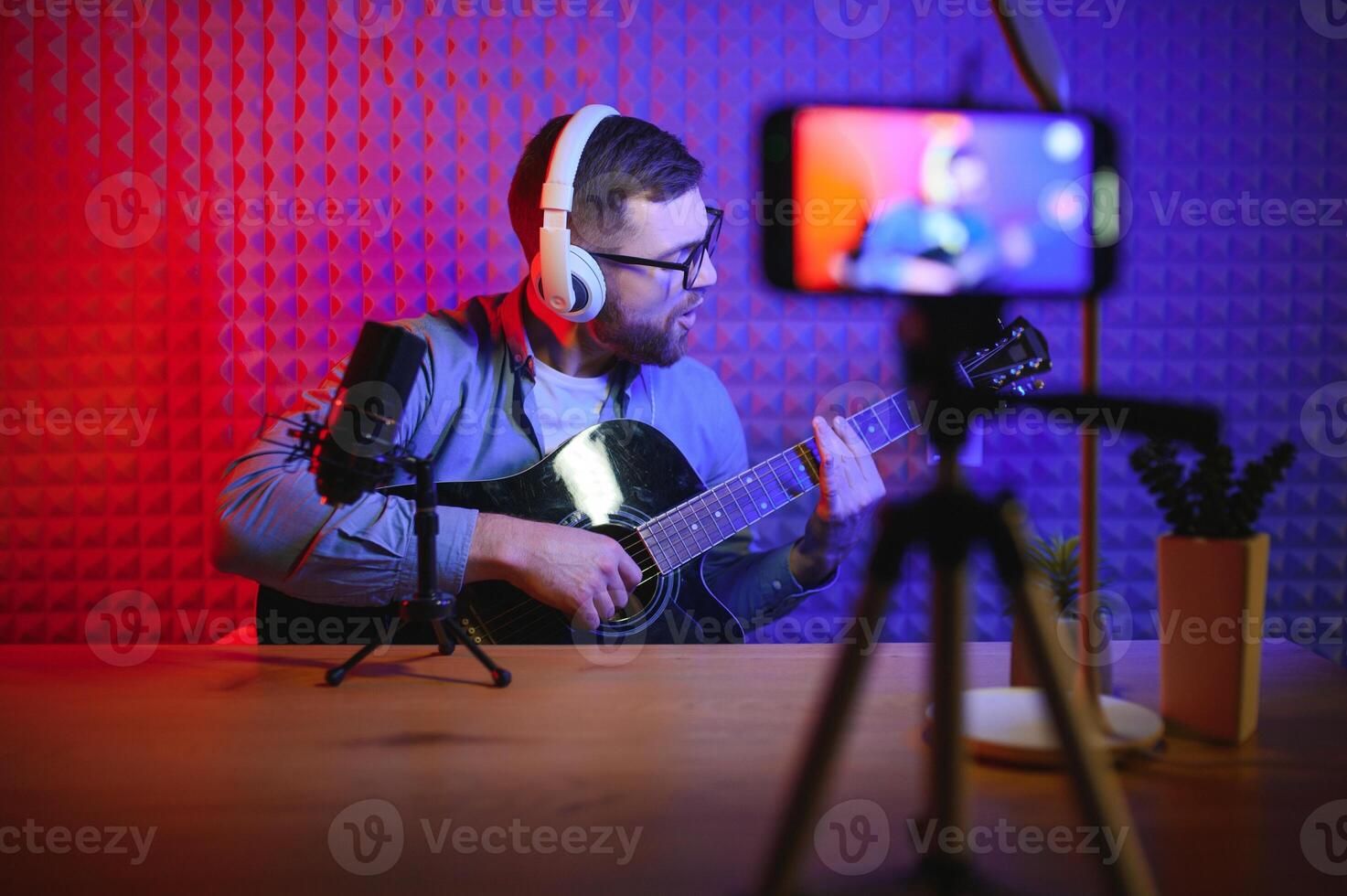 A young stylish guy with a beard wearing casual or music teacher playing guitar in front of smartphone camera. Online guitar training or vocal lesson photo