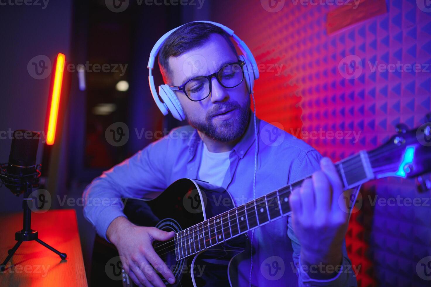 Close up man in headphones playing guitar and singing, recording on smartphone, musician artist recording new song for social network, blogger or music teacher shooting course in home studio photo