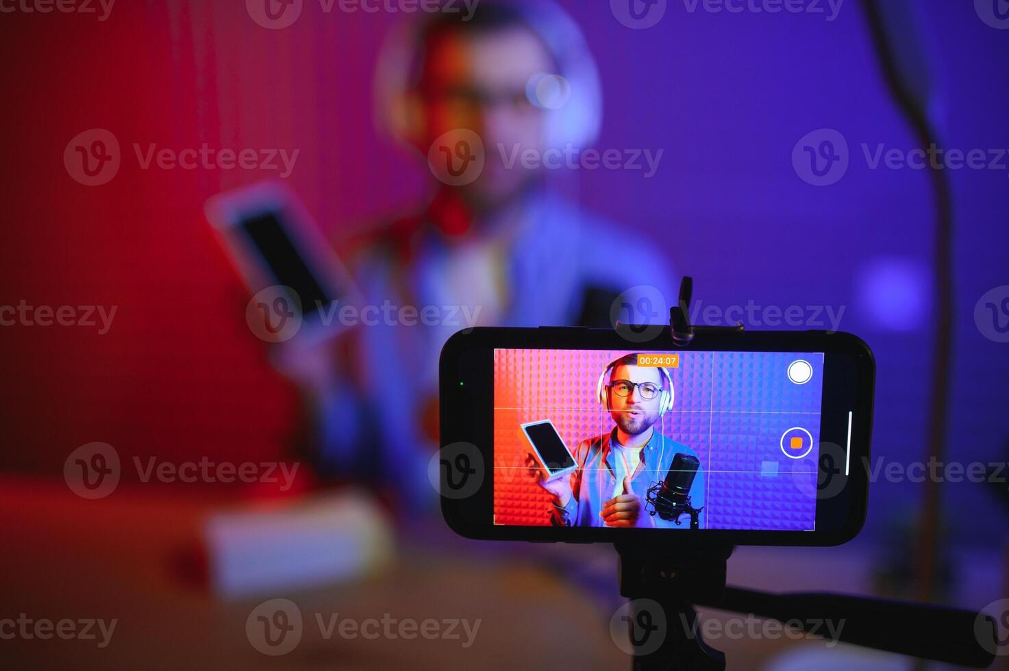Male technology blogger recording blog or vlog review of new smartphone, showing it on camera at home studio. Blogging, Work from Home concept. Selective focus. Web Banner photo