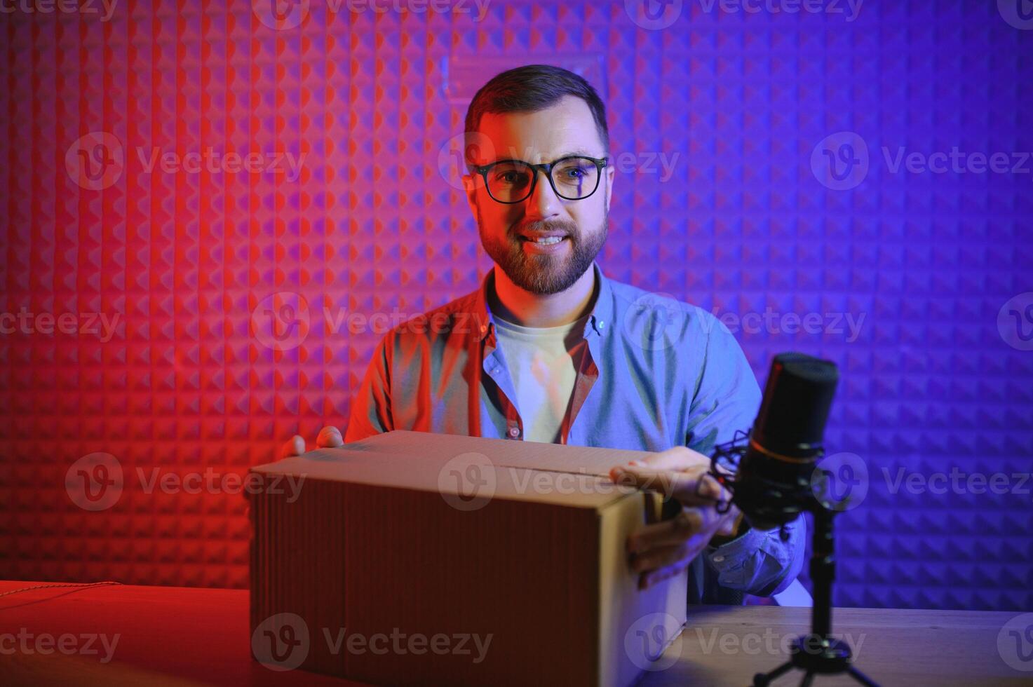 Panoramic view of young adult vlogger creating internet content, holding carton box in hands, unpacking received pack and recording media online on broadcast equipment photo