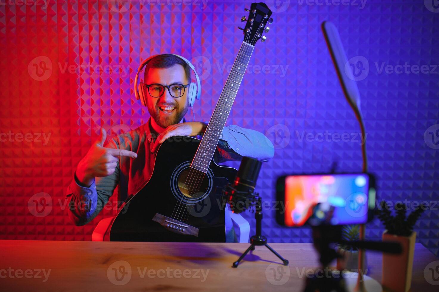 A young stylish guy with a beard wearing casual or music teacher playing guitar in front of smartphone camera. Online guitar training or vocal lesson photo