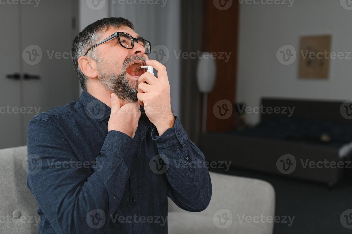 Mature man using an antiseptic throat spray at home photo