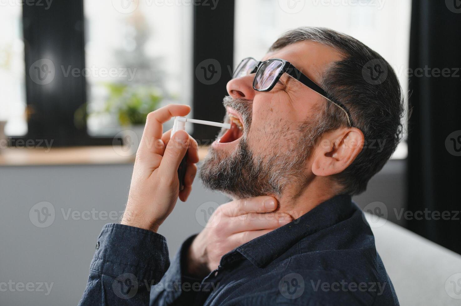 Sick senior man using throat spray at home photo