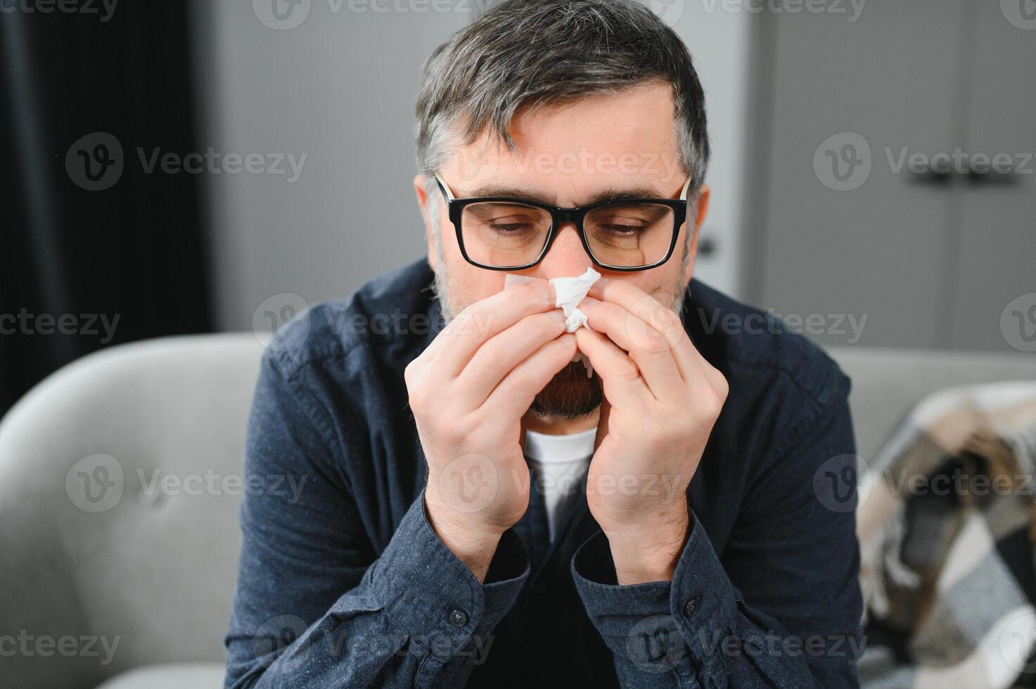 healthcare, flu, hygiene and people concept - sick senior man with paper wipe blowing his nose at home photo