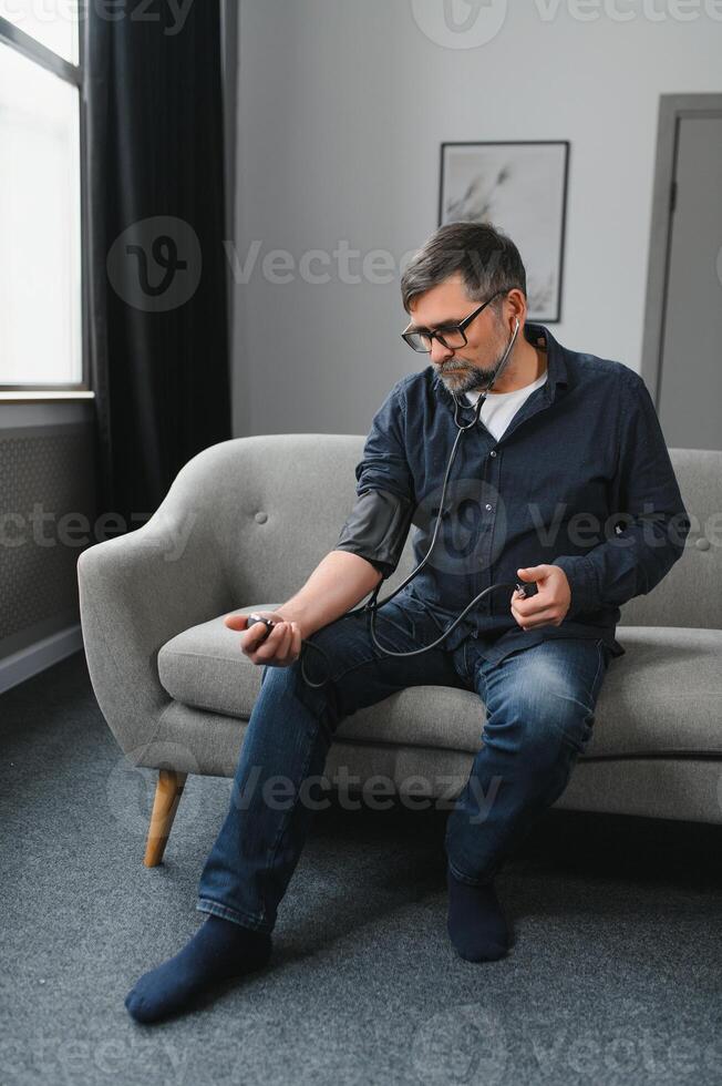 Senior caucasian retired male taking blood pressure at home photo