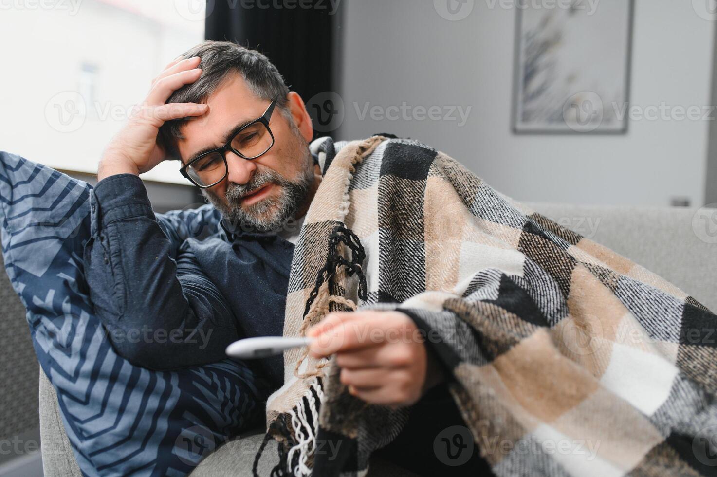 Sick senior man using thermometer checking his temperature suffering from seasonal flu or cold. photo