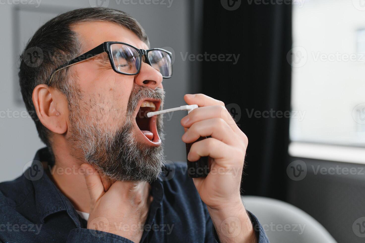 Sick senior man using throat spray at home photo
