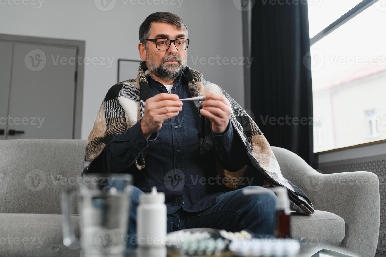 Sick senior man using thermometer checking his temperature suffering from seasonal flu or cold. photo