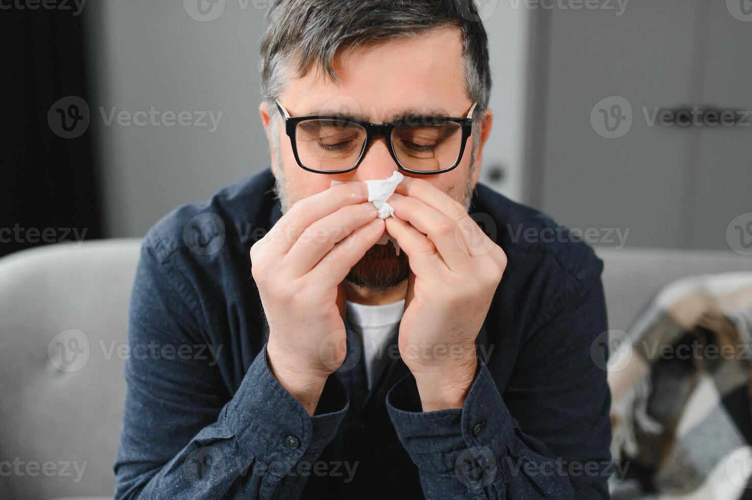 Middle age man feeling sick with cold and fever at home, ill with flu disease sitting on the sofa photo