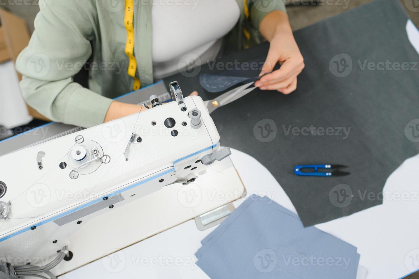 Cheerful young seamstress sits at the table with working things, in atelier photo