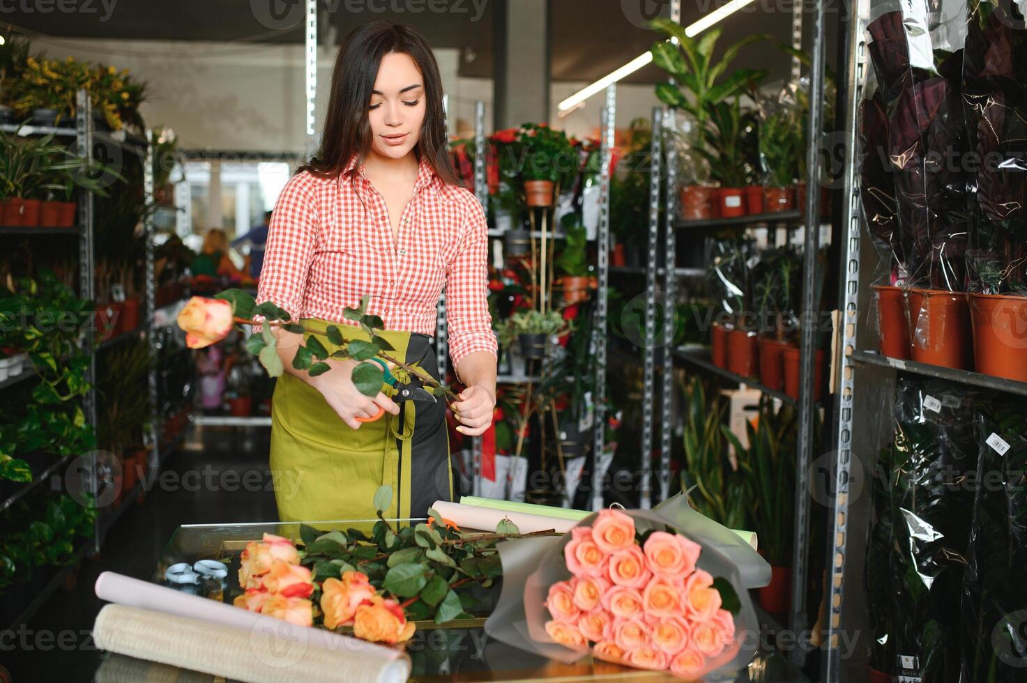 Cute girl florist collects a bouquet of roses in a flower shop. A beautiful florist creates a composition of flowers. Girl cuts flowers and removes stale leaves photo