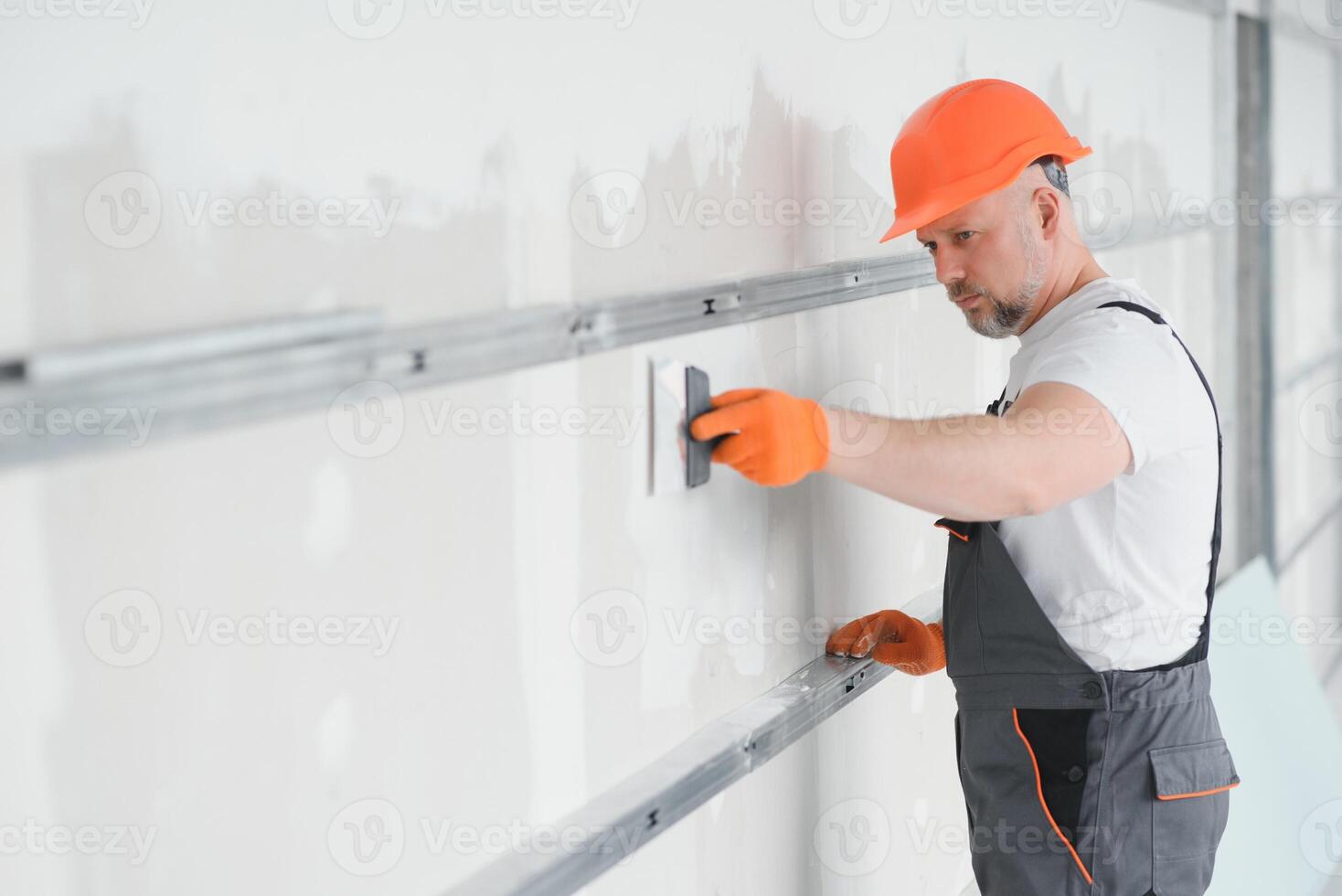 man drywall worker using trowel for plasterer putting stucco on plasterboard white wall. photo