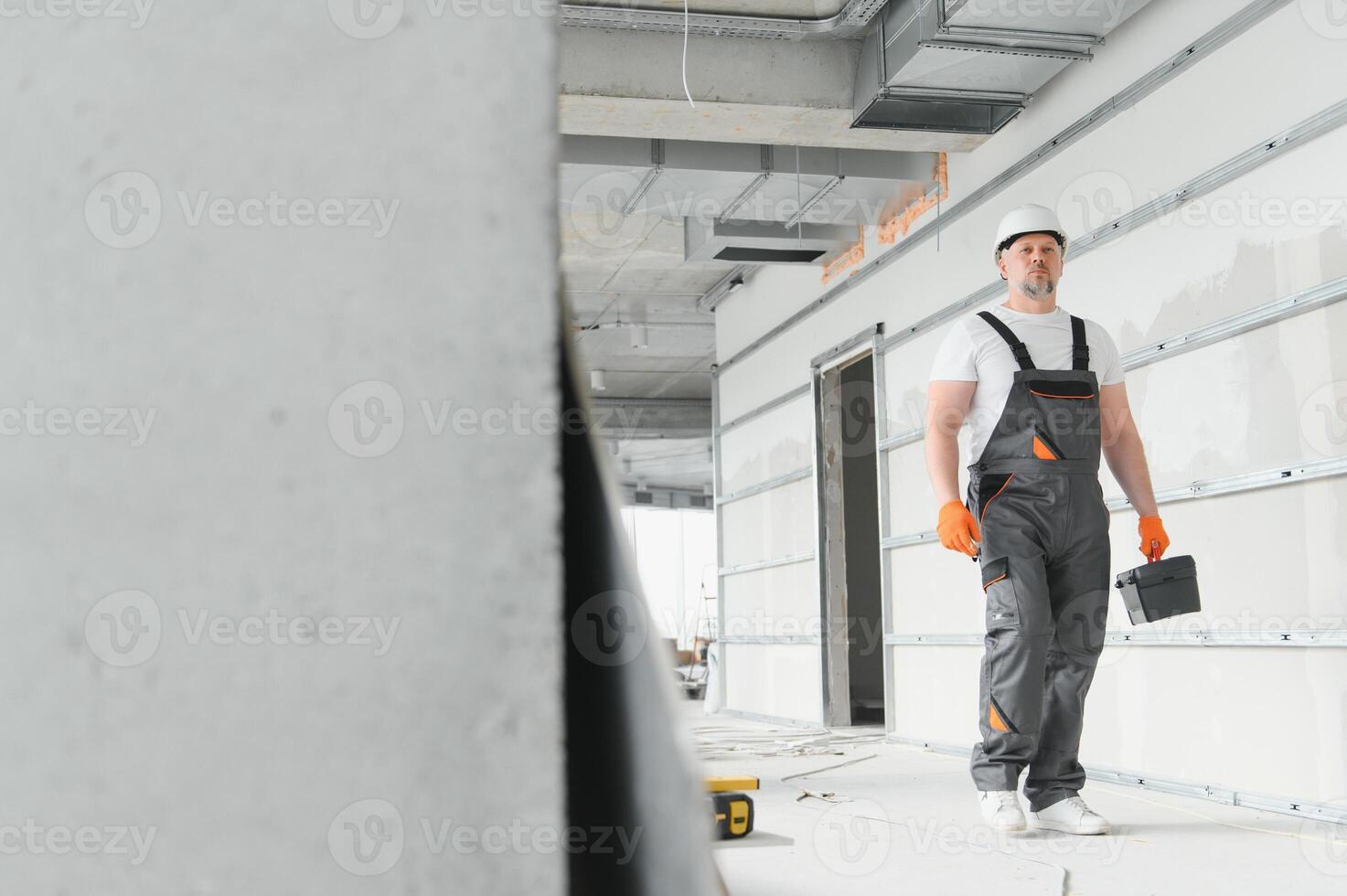 Portrait of a builder in working uniform with protective helmet standing with instruments at the construction site indoors photo