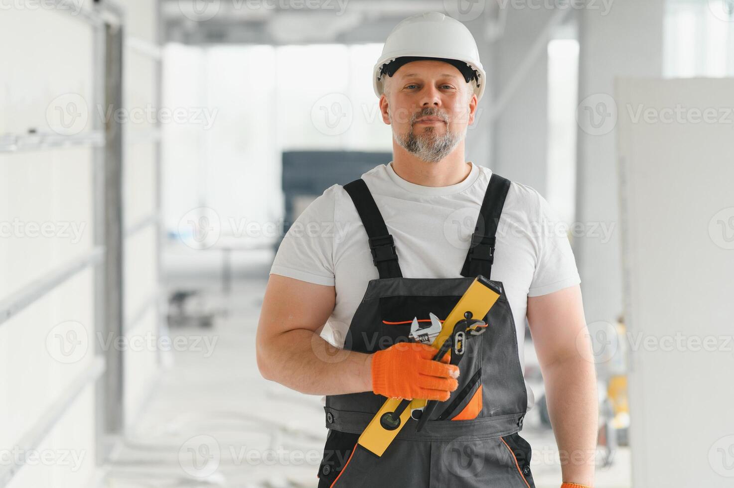 Portrait of a builder in working uniform with protective helmet standing with instruments at the construction site indoors photo