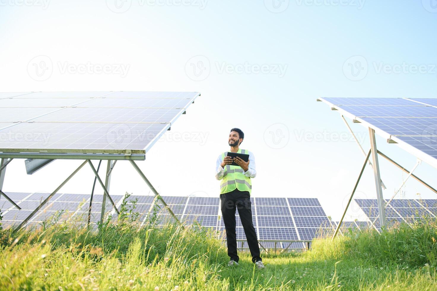 male engineer checks a photovoltaic solar plant and uses a recording tablet. Indian Man in uniform holding tablet. photo