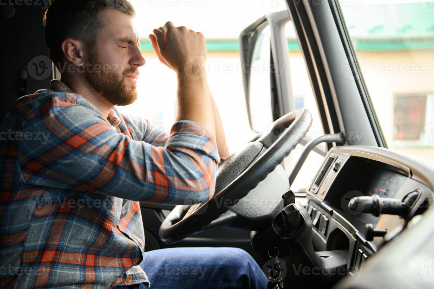 Tired of work. Sitting in the cabin. Young truck driver is with his vehicle at daytime. photo