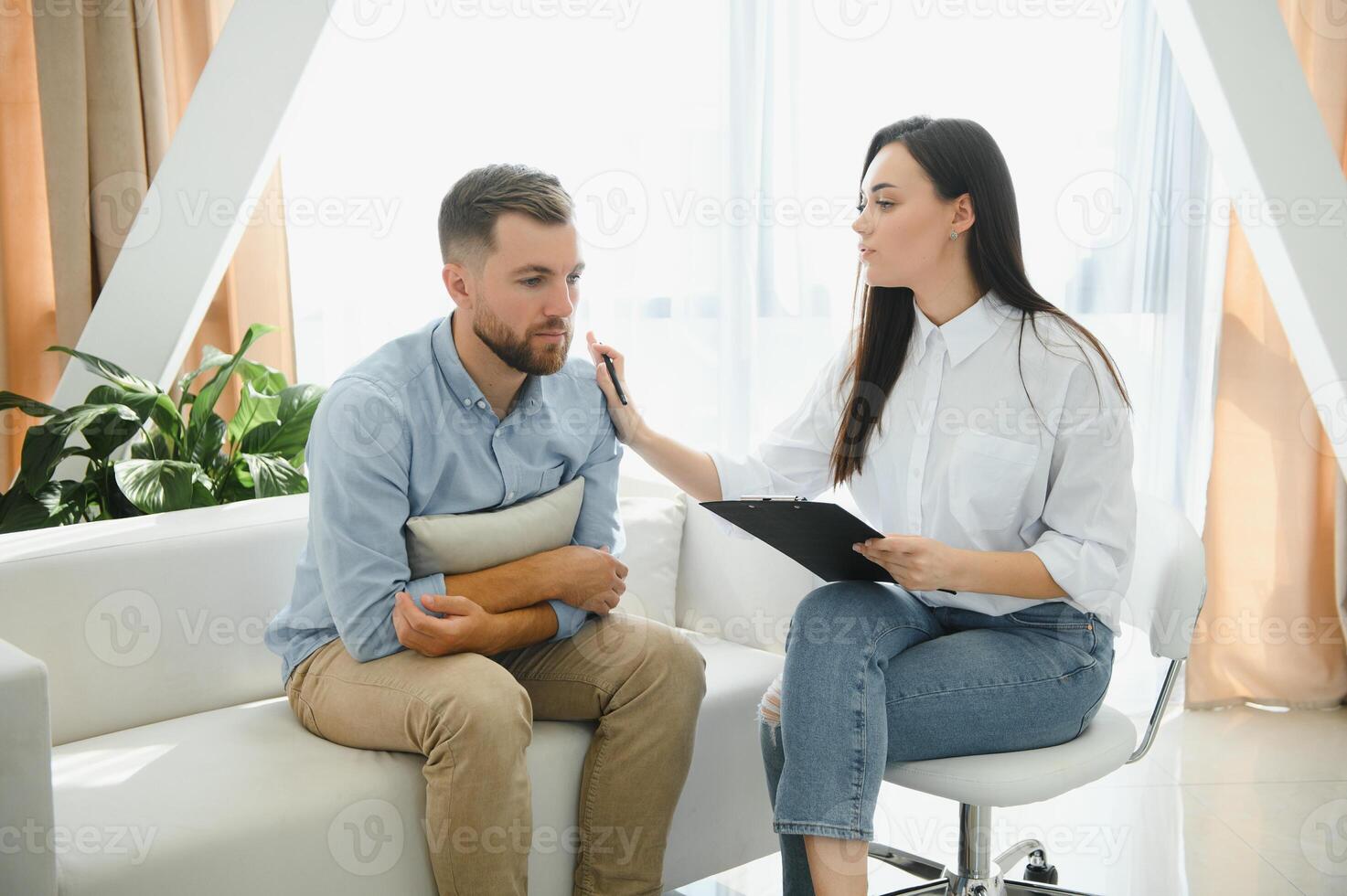 Psychologist talking with patient on therapy session. Depressed man speaking to a therapist while she is taking notes photo