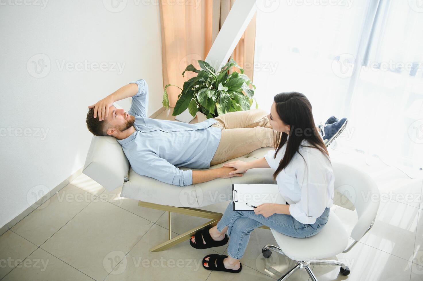 Session with a psychologist, psychotherapist. Young depressed male patient and professional female doctor with note pad. Lifestyle. Mental health care. photo
