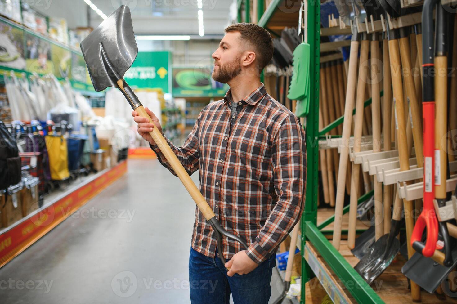 Portrait of a happy young man and customer buying a shovel while shopping at the hardware store photo