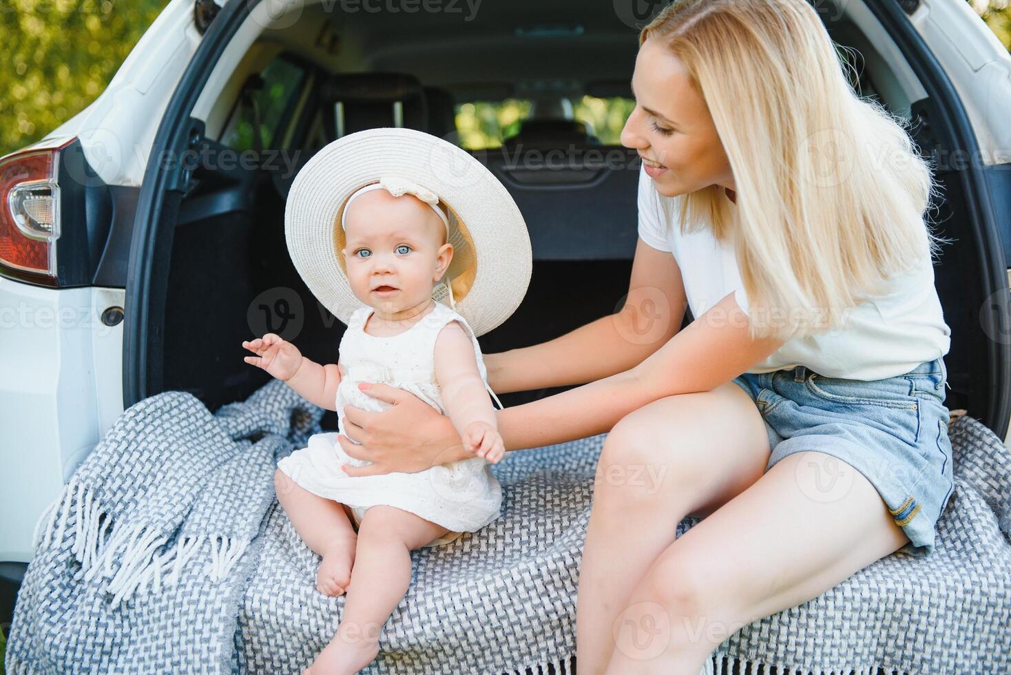Pretty young married couple and their daughter are resting in the nature. The woman and girl are sitting on open car boot. photo