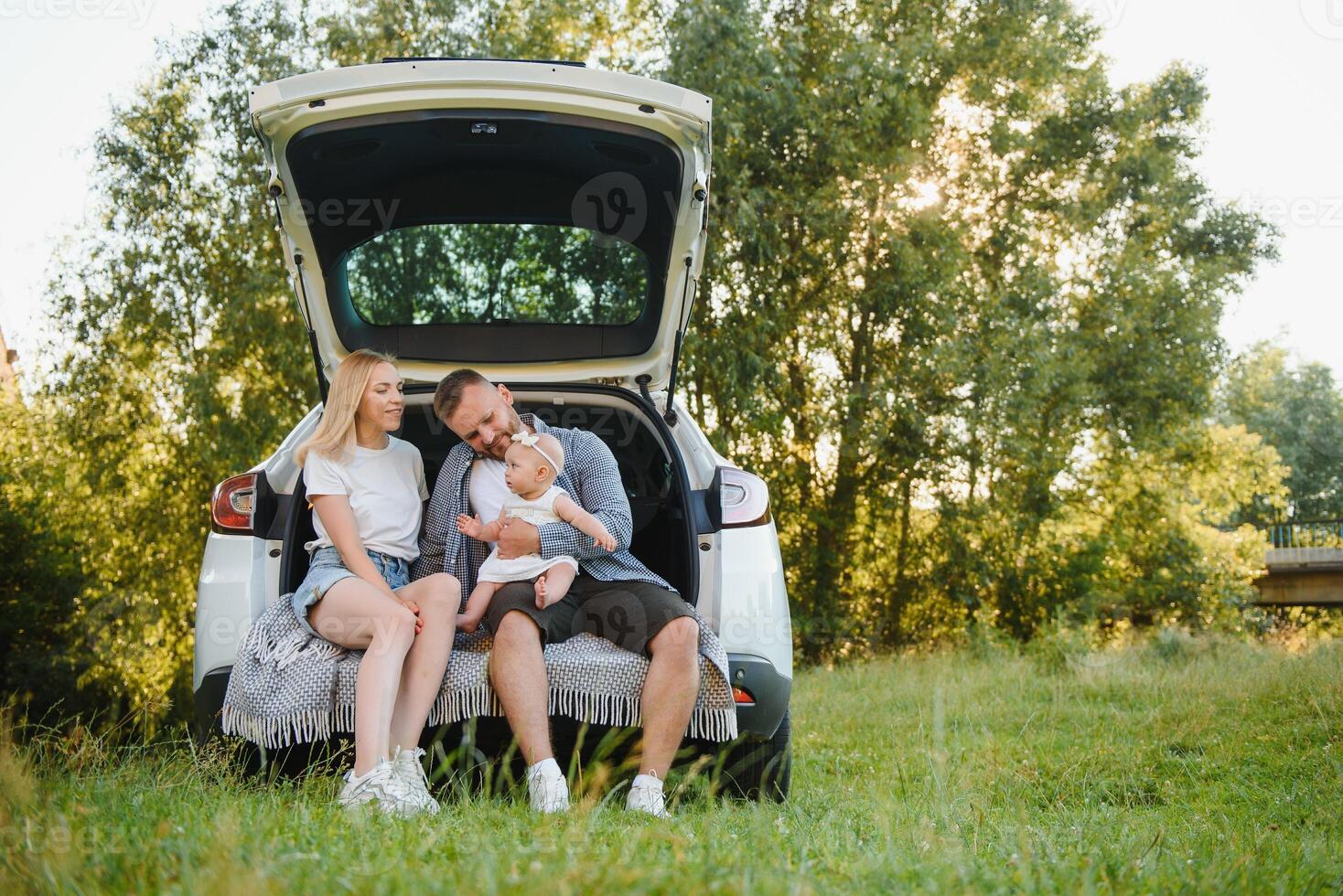 Young family three people in white clothes have picnic. Beautiful parents and daughter travel by car during summer vacation. photo