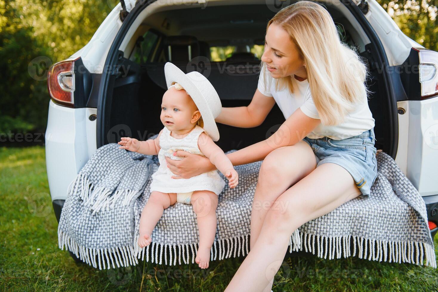 Pretty young married couple and their daughter are resting in the nature. The woman and girl are sitting on open car boot. photo