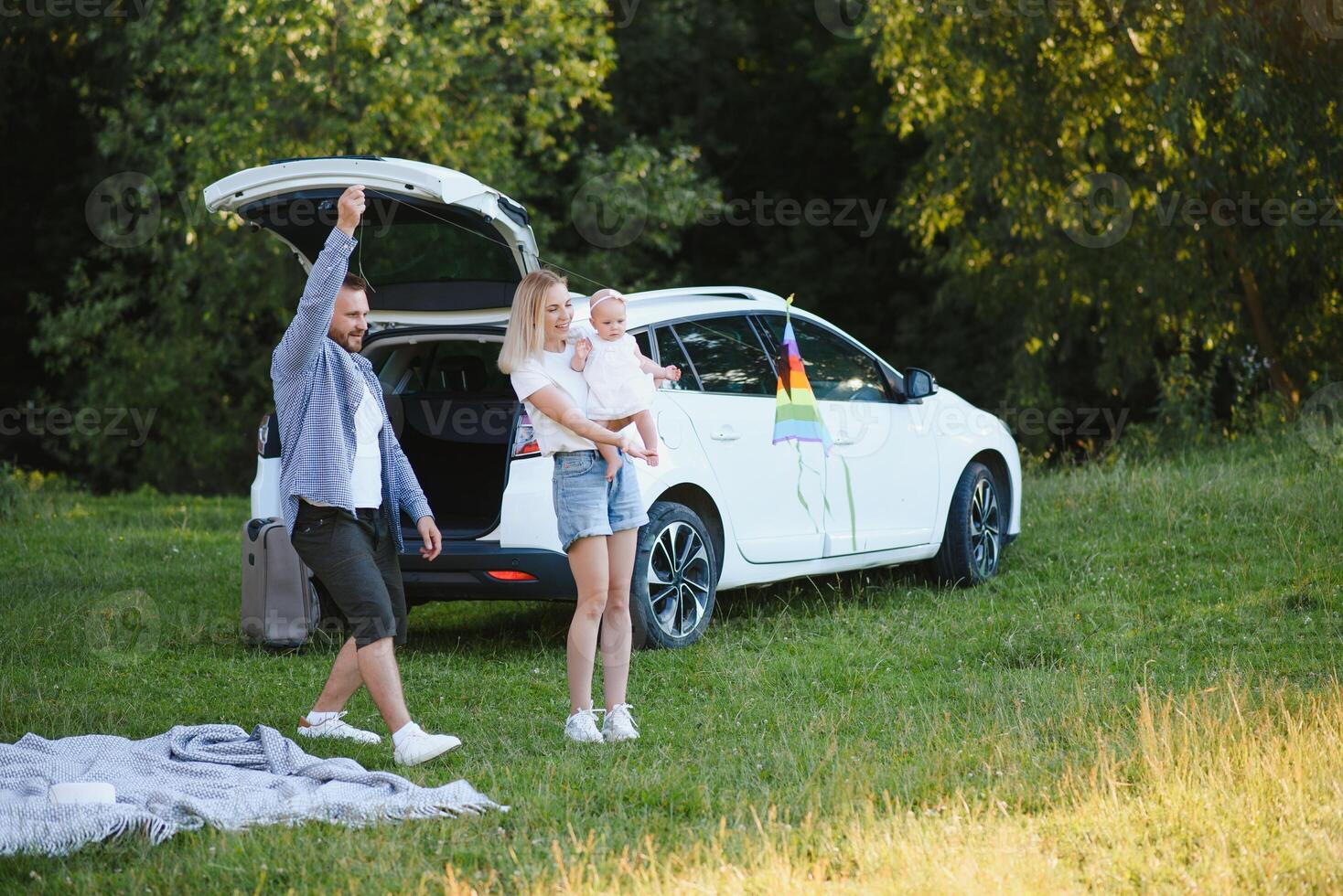 Young family three people in white clothes have picnic. Beautiful parents and daughter travel by car during summer vacation. Scene in park photo