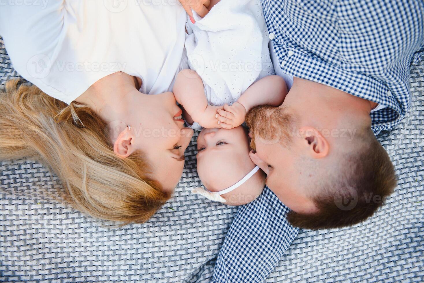 Mom, dad and little son lying on the blanket in the summer park. The concept of summer holiday. Mother's, father's, baby's day. Family spending time together on nature. Family look photo