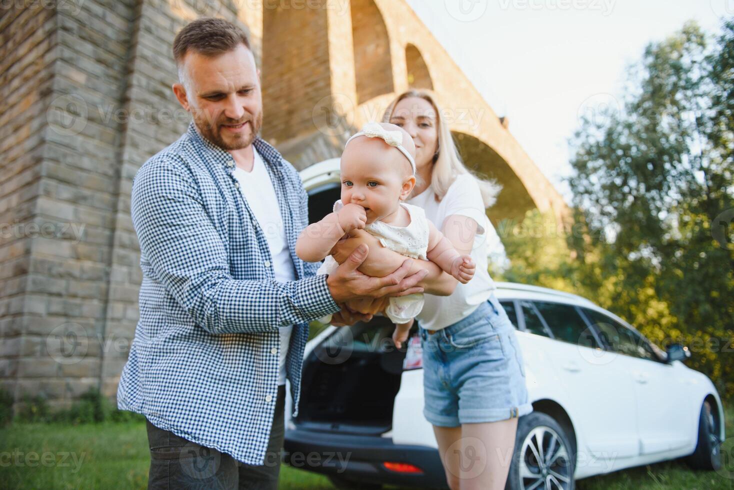 Young family three people in white clothes have picnic. Beautiful parents and daughter travel by car during summer vacation. Scene in park photo