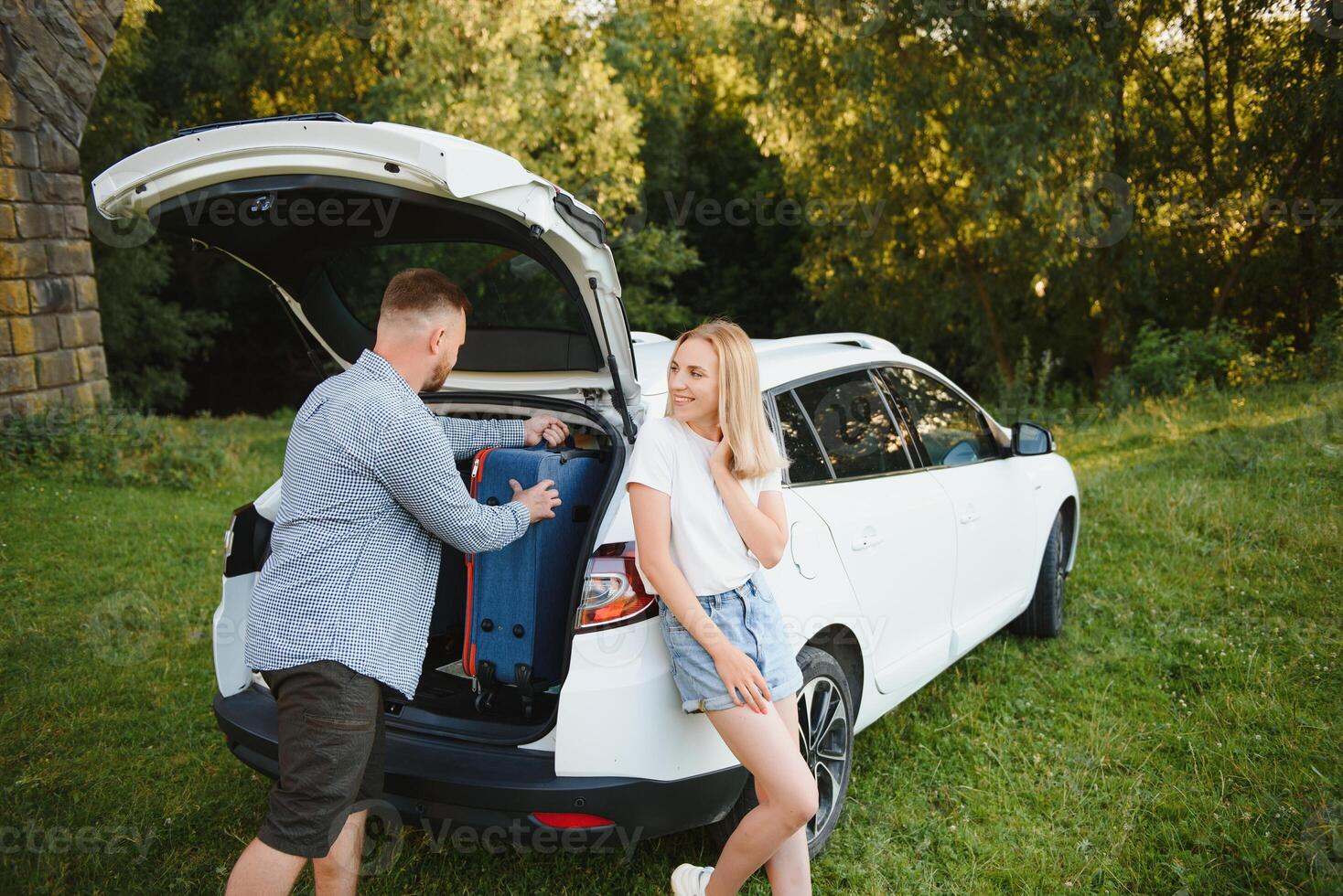 Young couple standing near the opened car boot with suitcases. photo