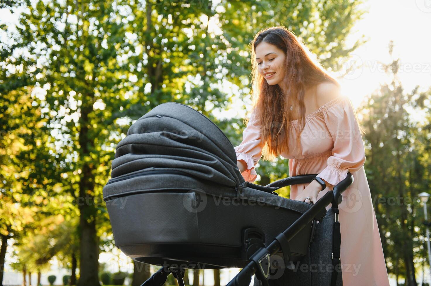 family, child and parenthood concept - happy mother walking with baby stroller in park. photo