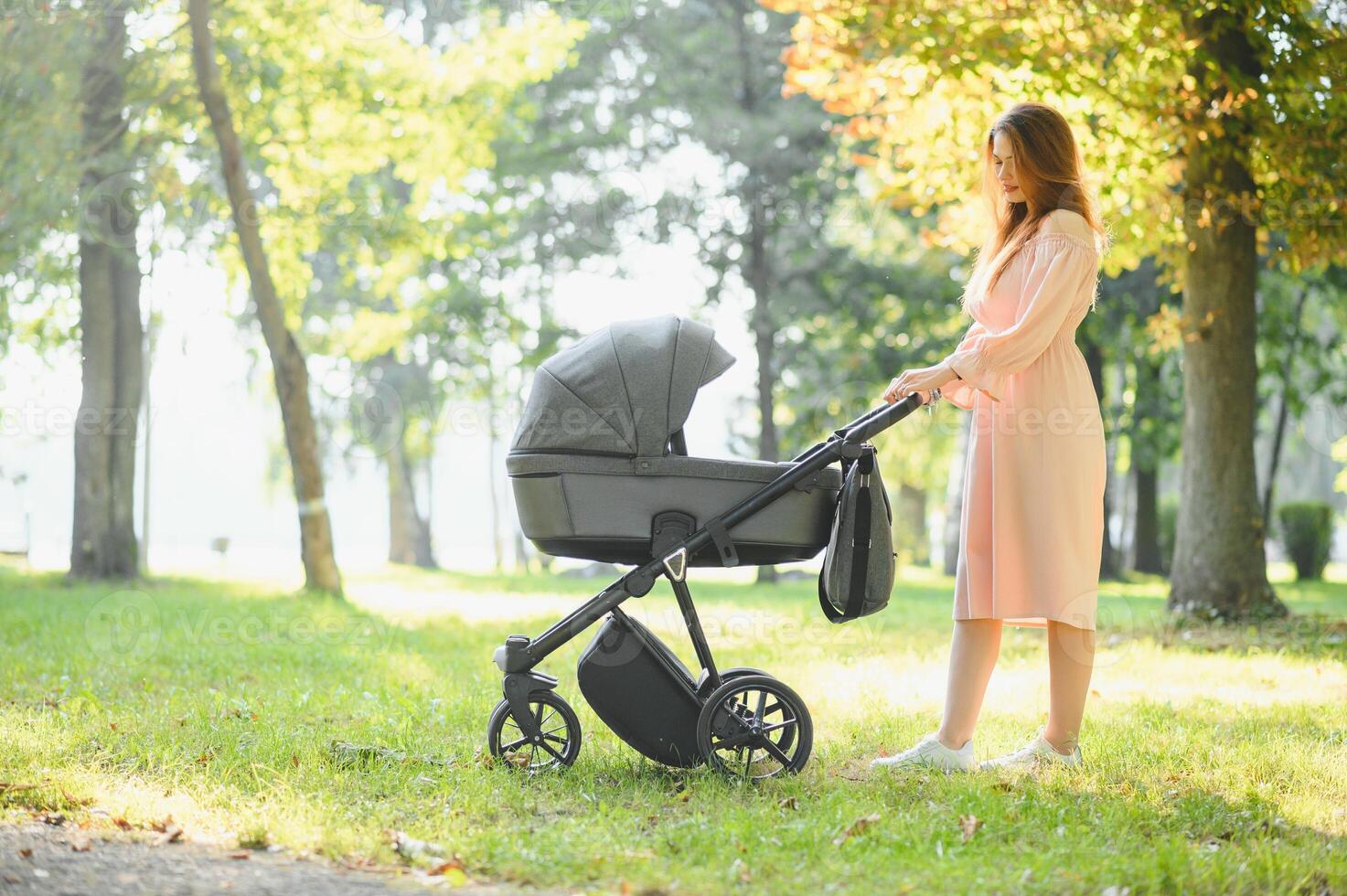 Happy young mother with baby in buggy walking in autumn park photo