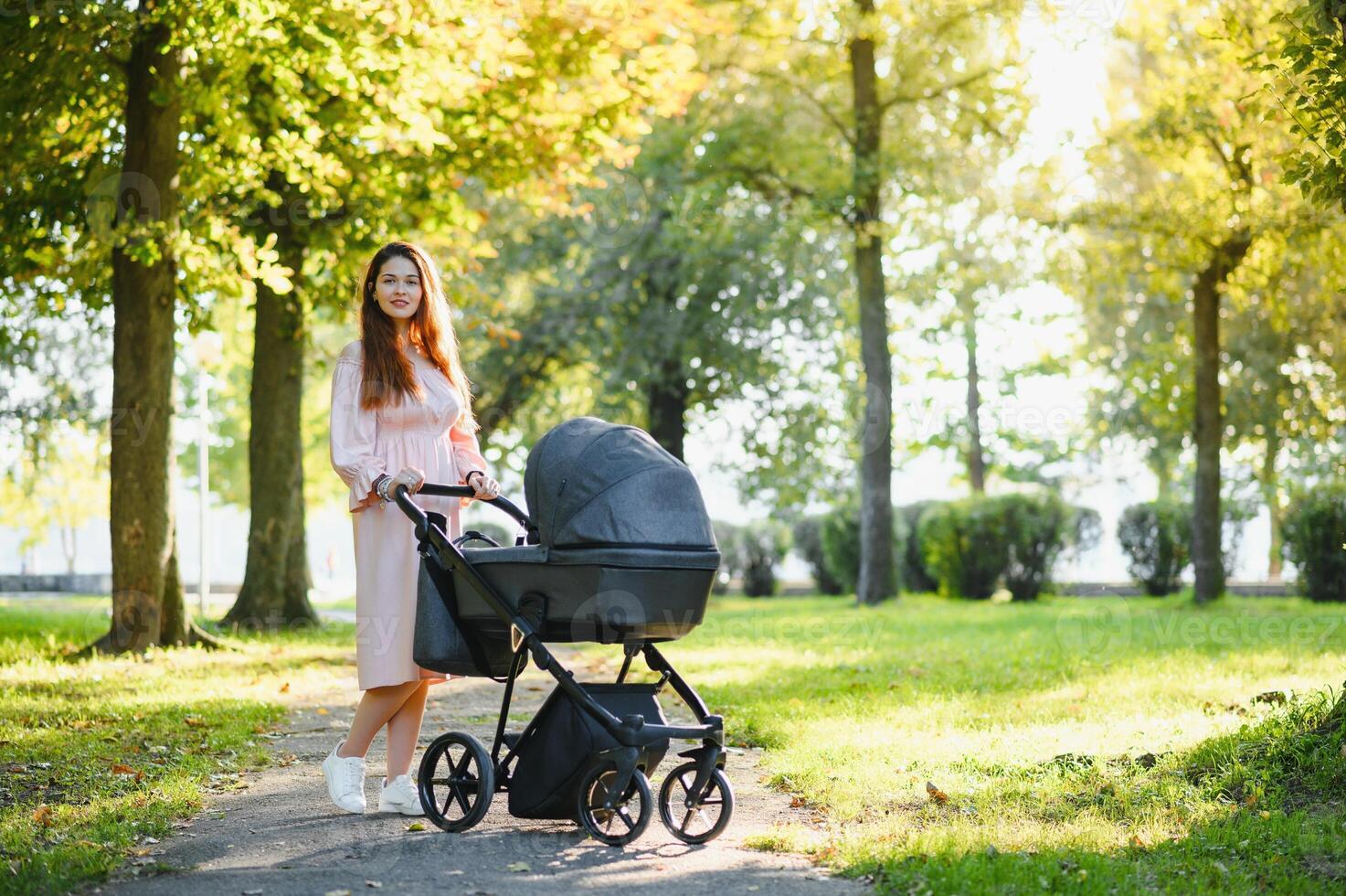 Happy young mother with baby in buggy walking in autumn park photo
