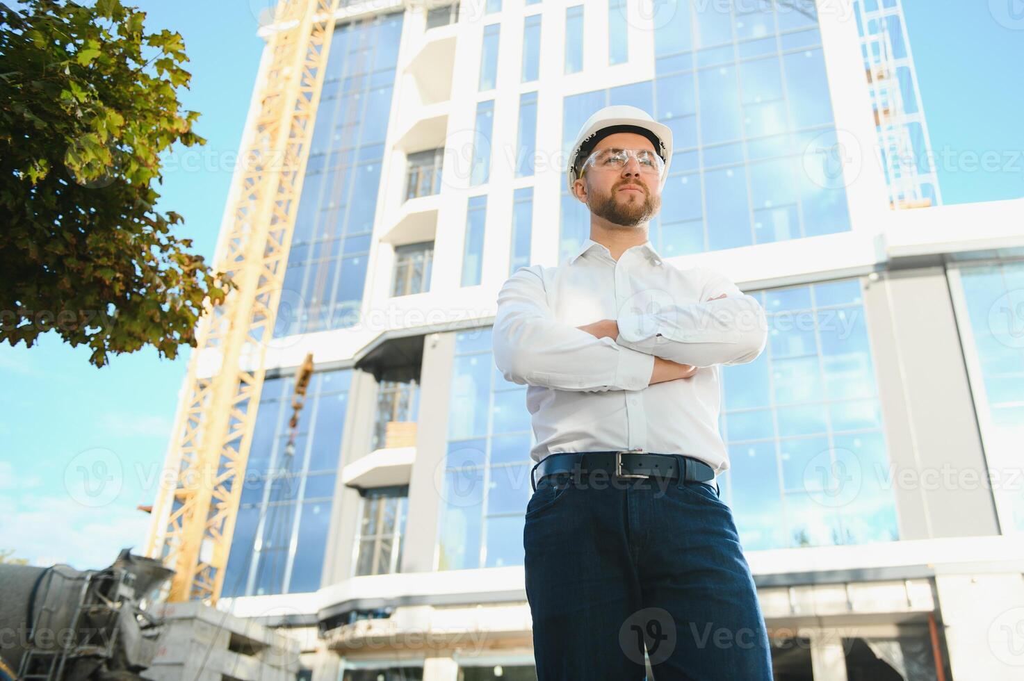 Successful engineer or architect, crane and building construction at backgrpound. Joyous businessman wearing helmet photo