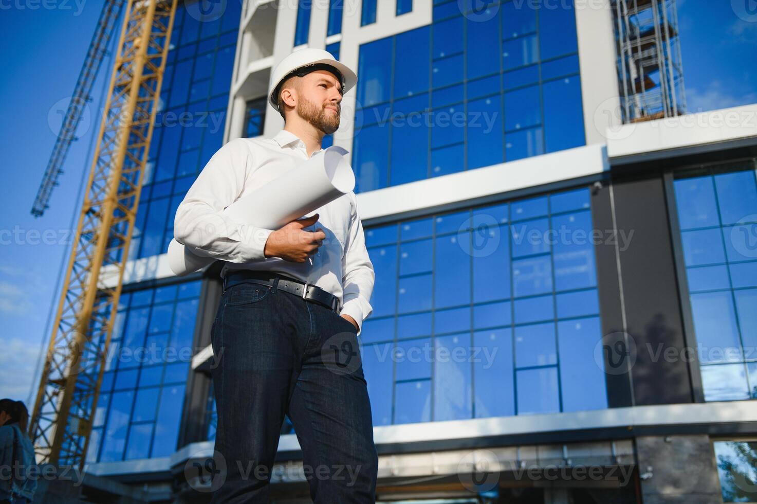 Successful engineer or architect, crane and building construction at backgrpound. Joyous businessman wearing helmet photo
