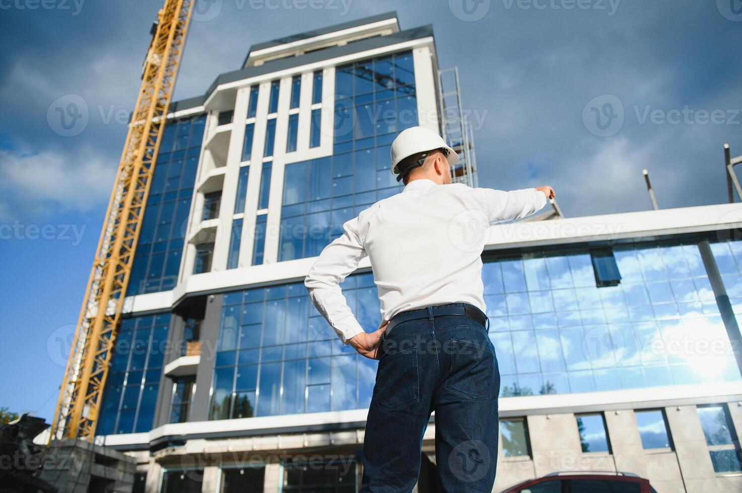 Successful engineer or architect, crane and building construction at backgrpound. Joyous businessman wearing helmet photo