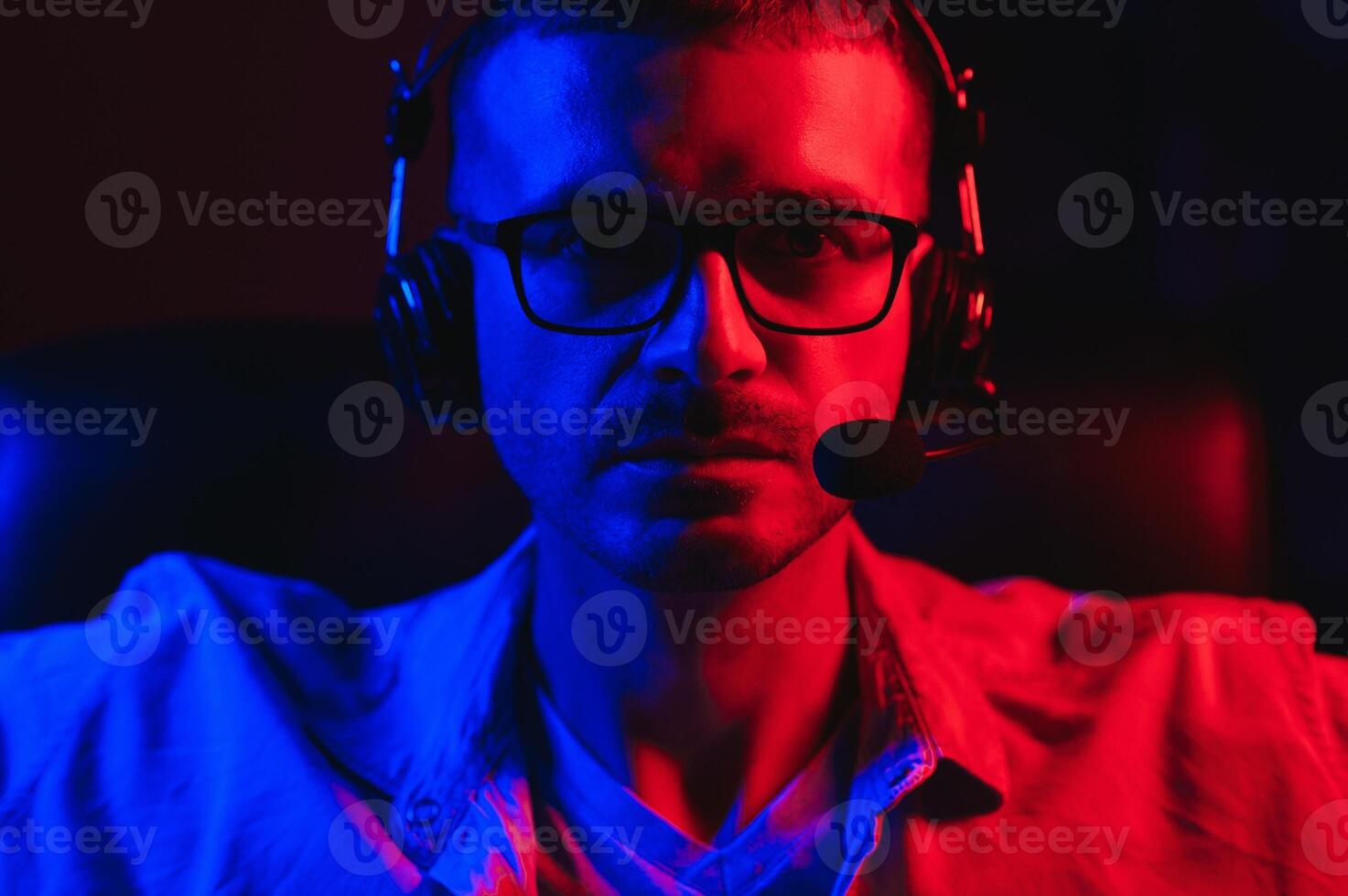 Professional Gamer Plays Game on His Computer. He's Participating in Online Cyber Games Tournament or in Internet Cafe. He Wears Glasses and Talks into Microphone. photo