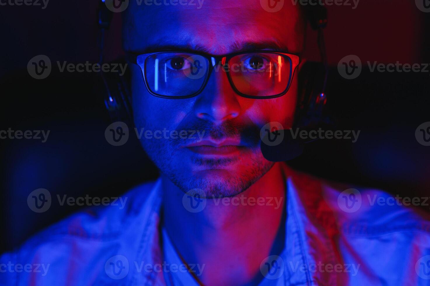 Professional Gamer Plays Game on His Computer. He's Participating in Online Cyber Games Tournament or in Internet Cafe. He Wears Glasses and Talks into Microphone. photo