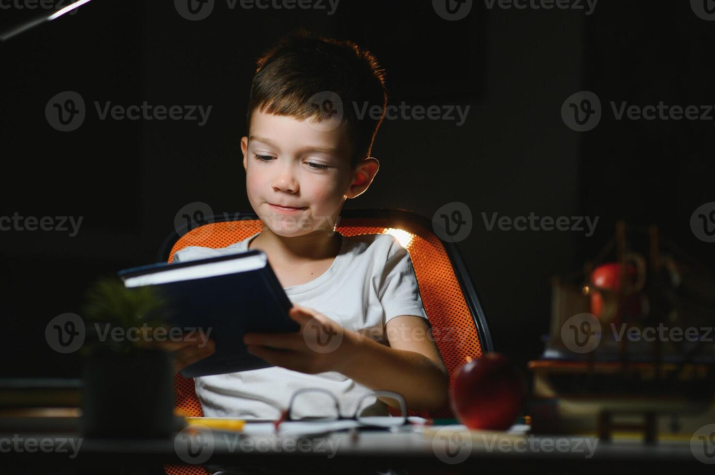 Boy learn lessons in the home setting at the table in the light of a table lamp. photo